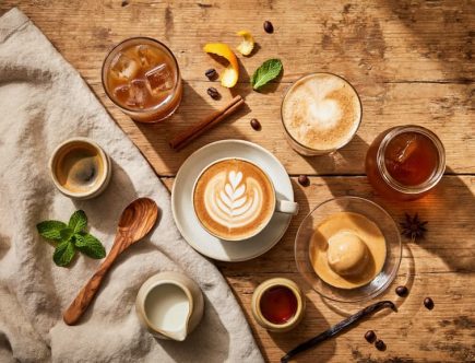 Vue du dessus d'une table en bois avec six boissons café différentes : expresso, café glacé, latte art, frappé, affogato et cold brew, entourés de grains de café, épices et ustensiles, ambiance boho estivale