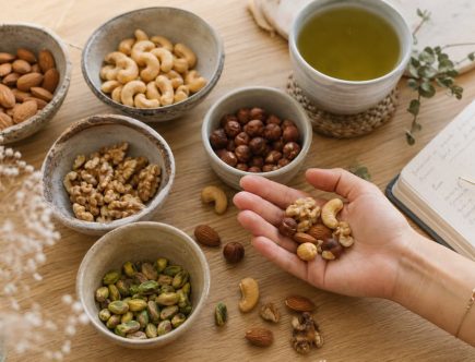 Bols de fruits secs variés (amandes, noix, cajou, noisettes) sur une table en bois avec une poignée dans une main