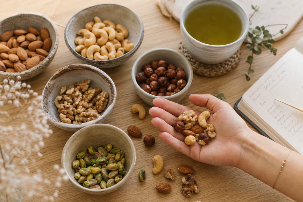 Bols de fruits secs variés (amandes, noix, cajou, noisettes) sur une table en bois avec une poignée dans une main