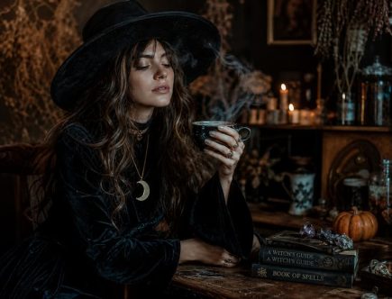 Déguisement d'Halloween boho-chic avec robe noire vintage, chapeau et bougies dans une ambiance sombre