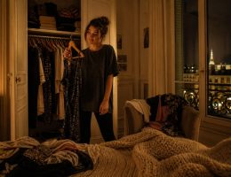 Femme en panique devant son dressing ouvert un samedi soir, vêtements éparpillés, ambiance dorée et chaleureuse