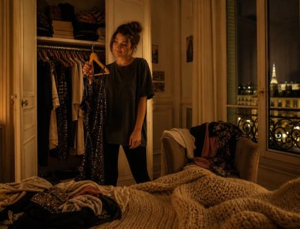 Femme en panique devant son dressing ouvert un samedi soir, vêtements éparpillés, ambiance dorée et chaleureuse